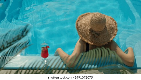 Teenage girl in a straw hat relaxing by the pool, with palm leaves gently swaying in the foreground - Powered by Shutterstock