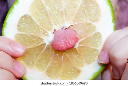 A teenage girl stuck her tongue through the hole in the middle of a sliced Citrus Sweetie. Close-up, selective shot.