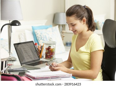 Teenage Girl Studying At Desk In Bedroom Using Mobile Phone