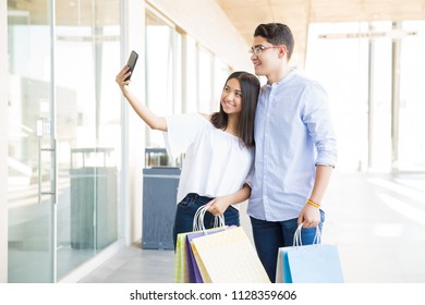 Teenage Girl Taking Selfie With Boyfriend On Smartphone While Hanging Out In Shopping Mall