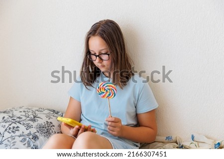 Teenage girl talks on the phone with a lollipop in her hand sitting on the bed