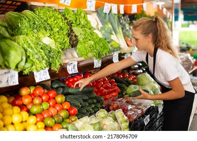 Teenage Girl In Uniform Working In Grocery Shop As First Job Experience, Selling Cucumber