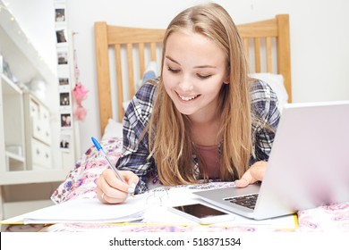 Teenage Girl Using Laptop To Do Homework In Bedroom