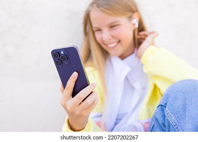 Teenage girl using mobile phone and listening to music on wireless earbuds - Shutterstock ID 2207202267