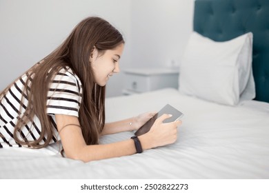 Teenage Girl Using Tablet in a Comfortable Bedroom. A teenage girl with long brown hair lying on a bed while using a tablet. - Powered by Shutterstock