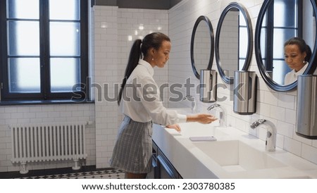 Teenage girl wash hands in school toilet and chat. Side view of diverse teen students washing hands in campus bathroom