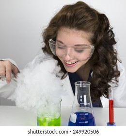 Teenage Girl Wearing Lab Coat And Doing A Science Experiment With Green And Blue Liquid In Tubes And Tongs.