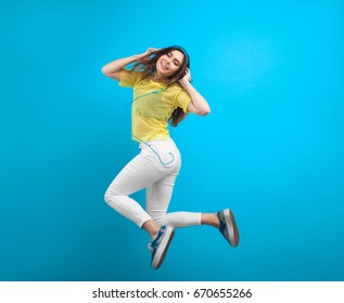 Teenage Girl Wearing Sneakers White Pants And Sheer Shirt Jumping Against Turquoise Background. 