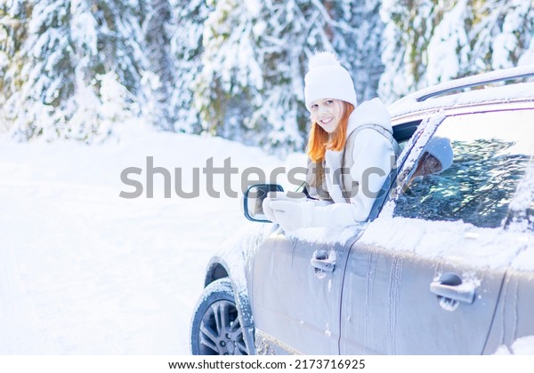 teenage girl\
in white sweater, vest and white knitted hat in car window in snowy\
forest having fun, concept of winter local travel during Christmas\
or New Year holidays and\
vacations