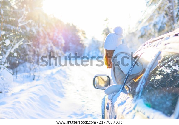 teenage girl\
in white sweater, vest and white knitted hat in car window in snowy\
forest having fun, concept of winter local travel during Christmas\
or New Year holidays and\
vacations