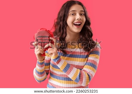 Teenage girl with whoopee cushion on red background. April Fools' Day celebration
