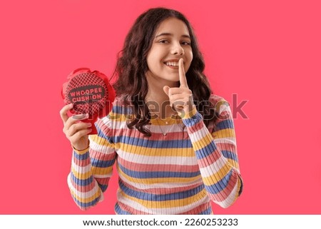 Teenage girl with whoopee cushion showing silence gesture on red background. April Fools' Day celebration