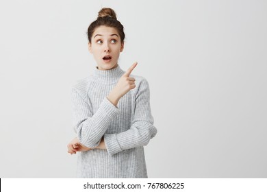 Teenage girl with wonder looking to side and showing with index finger. Curious female employee trying to pay attention over white background. Attention concept