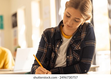 Teenage girl writing in notebook, studying attentively in high school classroom. Education, focusing, learning, teenager, student, homework - Powered by Shutterstock