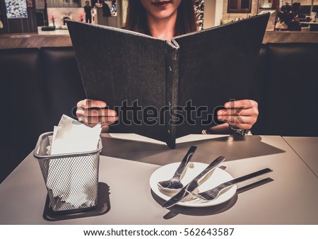 Teenage girl or young woman Choosing Looking from a Restaurant Menu deciding what to order . Breakfast and dinner . Customize colors Vintage retro and old film Tone 