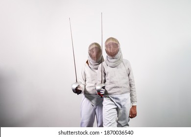 Teenage girls in fencing costumes with swords in their hands isolated on white studio background. Young people practice and practice fencing. Sports, healthy lifestyle.