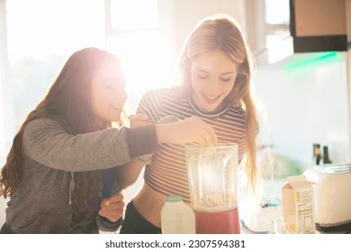 Teenage girls making smoothie in sunny kitchen - Powered by Shutterstock