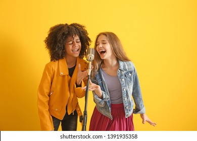 Teenage girls with microphone singing against color background