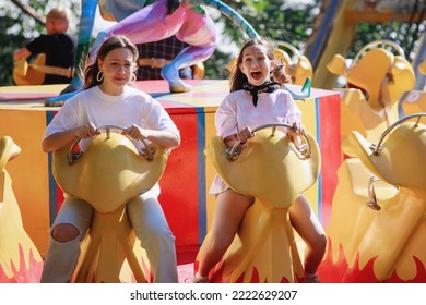 Teenage girls ride on carousels in the park. Emotional explosion, fear of falling, shock at high speed. Selective focus, blurred background. - Powered by Shutterstock