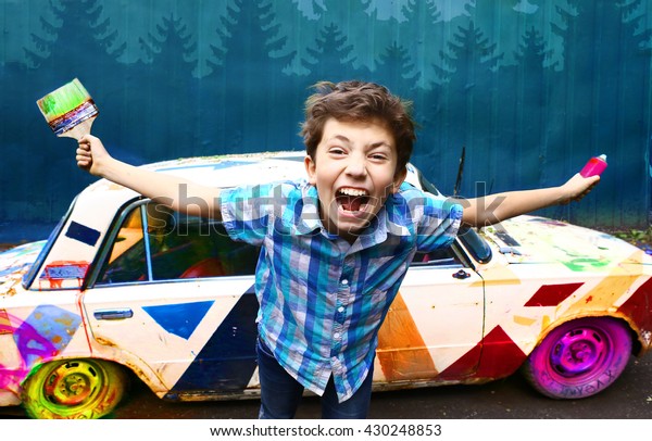 teenage handsome boy with brush and graffiti\
spray on the old painted retro car background closeup portrait on\
the blue wall\
background