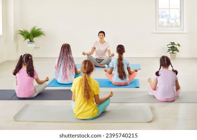 Teenage kids girls sitting back on the floor with female teacher couch or trainer relaxing in gym sitting on yoga mat in Lotus pose meditating and doing yoga exercise. Children sport workout concept. - Powered by Shutterstock