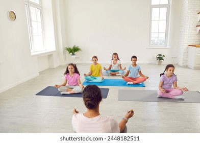 Teenage kids girls sitting on the floor with female teacher couch relaxing in gym sitting on yoga mat in Lotus pose meditating and doing yoga exercise. Children sport workout concept. - Powered by Shutterstock