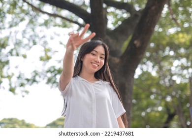 A Teenage Lady Holding Up A Peace Sign As She Does A Wacky Pose At The Camera While Strolling At The Park.