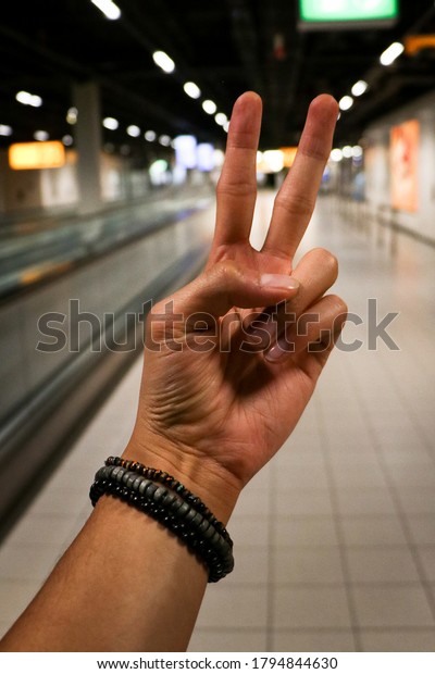 Teenage man holding a peace\
and love sign with his hand. Travel, tourism. Bracelets, light\
brown skin.