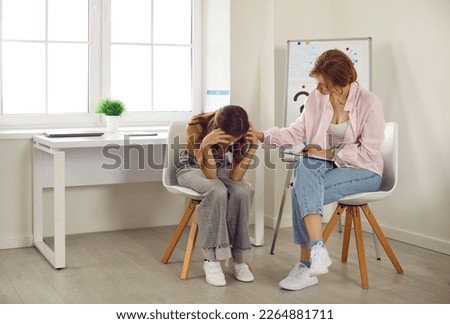 Teenage problems. Female school psychologist supporting sad teenage girl during her difficult situation at school. Female psychologist touches shoulder of teenage girl who sadly bowed her head.