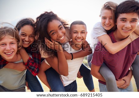 Teenage school friends having fun piggybacking outdoors