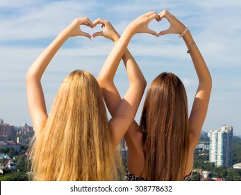 Teenage sisters holding hands together.Two female friends holding hands up in summer.Two young woman making heart shape with hands.Two young girl friends standing together,having fun.Amazing city view