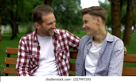 Teenage Son Talking With Father On Bench, Telling Secrets And Smiling, Trust