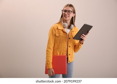 Teenage student with tablet, folder and headphones on beige background - Powered by Shutterstock