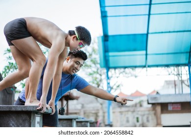 teenage swimmer standing on block board and getting ready to jump and swim with a coach - Powered by Shutterstock