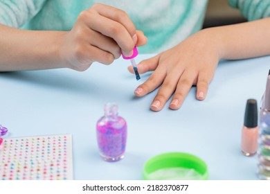 Teenage Woman Painting Her Nails At Home, With Nail Supplies On The Table