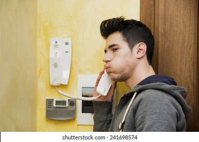 Teenager Answering The Intercom At The Entrance In An Apartment Blowing Out His Cheeks In Frustration On Finding An Unwelcome Visitor On The Other End