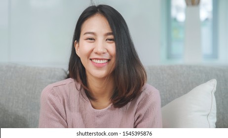 Teenager asiatische Frau fühlt sich glücklich, lächeln und schauen auf die Kamera, während sie sich im Wohnzimmer zu Hause entspannen. 