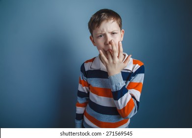 Teenager Boy Of About Ten European Appearance Brown Put His Finger In His Mouth On A Gray Background, Taste, Lick