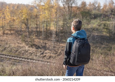 Teenager boy with backpack walking on path in autumn park. Active lifestyle, Back to school. Rear view of student boy in fall forest. People from behind