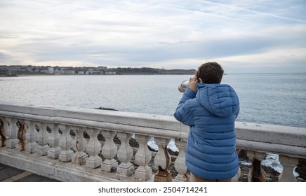 teenager boy with blue jacket looking through binoculars at the seaside - Powered by Shutterstock