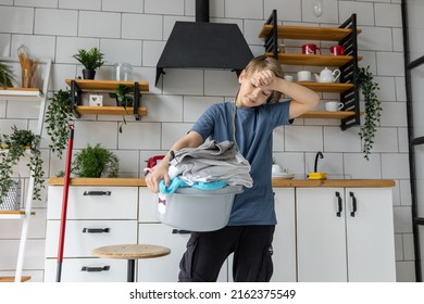 Teenager Boy Doing Chores, Cleaning, Sorting Laundry In The Kitchen At Home. Looking Tired And Unhappy