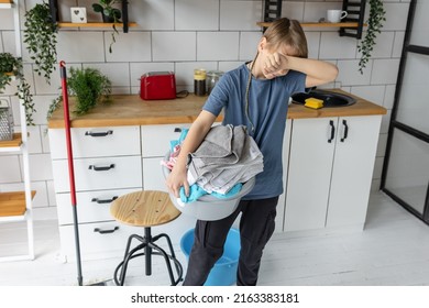 Teenager Boy Doing Chores, Cleaning, Sorting Laundry In The Kitchen At Home. Looking Tired And Unhappy