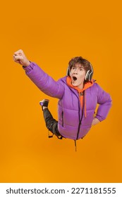 A teenager boy in fashionable bright clothes and headphones flies through the air. Lifestyle of the modern teenager. Studio yellow background with copy space.  - Shutterstock ID 2271181555