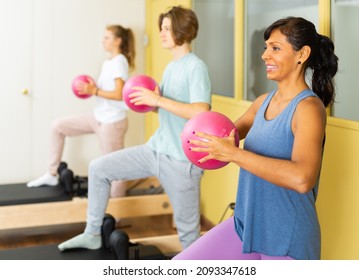 Teenager boy and girl exercising with pilates trainer latin woman in gym. They're standing in row and doing exercises with small fitness balls.