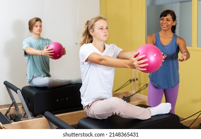 Teenager boy and girl exercising with pilates trainer latin woman in gym. They're training with pilates reformers and small fitness balls.
