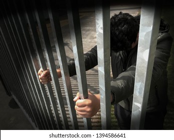 Teenager Boy Hands Holding Strong Iron Bars. Immigrant And Refugee Crisis In Europe, USA And Mexico. Seen From Above. Dramatic Border Fence Or Prison Concept 