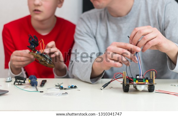 A teenager boy\
with his dad teacher collects a handmade robot working on the\
arduino platform. STEM education for children and teenagers,\
robotics and electronics. DIY. AI.\
STEAM.