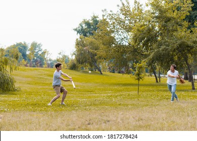 Teenager Boy Holding Softball Bat And Playing Baseball With Father In Green Park