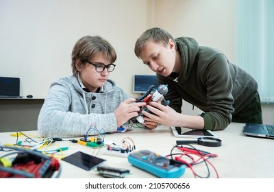 Teenager boy with instructor at robotics school makes robot managed from the constructor, child learns robot constructing.