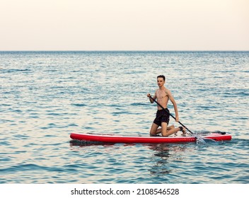 Teenager Boy Learning To Paddle On A SUP Board In The Sea Kneeling